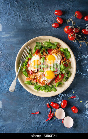 Traditionelle israelische Gerichte Shakshuka. Spiegelei mit Gemüse Tomaten und Paprika in Keramik Platte mit Kräutern und Zutaten oben über bl Stockfoto