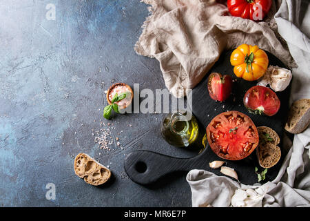 Vielzahl von roten und gelben Bio Tomaten mit Olivenöl, Knoblauch, Salz und Brot für Salat oder Bruschetta auf Holz Schneidebrett mit Leinen ove Stockfoto