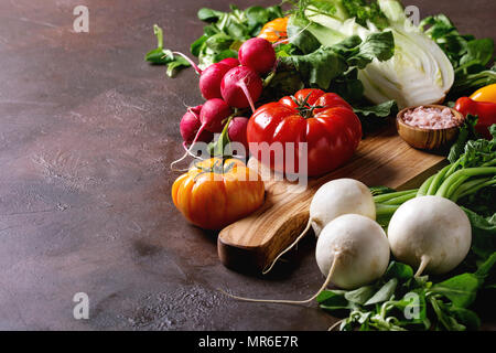 Vielzahl von nassen Rohe frische organische bunte Gemüse Tomaten, Radieschen mit Blättern, Fenchel, Paprika, Salz für Salat auf Holz Schneidebrett über Dunkel Stockfoto