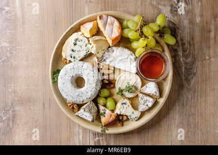 Käseplatte Sortiment an französischen Käse serviert mit Honig, Nüssen, Brot und Trauben auf Keramik Platte über Holz Textur Hintergrund. Ansicht von oben, Kopieren sp Stockfoto