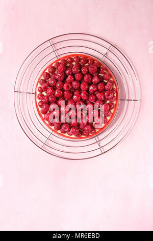 Rote Himbeere Butterkekse Tarte mit Zitrone Vanillesauce und verglaste frische Himbeeren auf Kühlung Rack über Rosa pastell Hintergrund serviert. Ansicht von oben, kopieren Raum Stockfoto