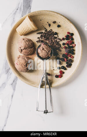 Hausgemachte Schokolade Himbeere Eis Kugeln mit gefrorenen Beeren serviert, gehackt dunkle Schokolade und Metalllöffel in Keramik Platte über weißem Marmor bac Stockfoto