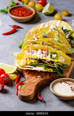 Auswahl an vegetarischen Mais Tacos mit Gemüse, Salat, Chili Pfeffer serviert auf Holz Schneidebrett mit Tomaten und Sahne Saucen mit ingredien Stockfoto