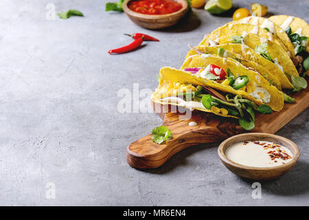 Auswahl an vegetarischen Mais Tacos mit Gemüse, grüner Salat, Chili in der Olive Holz Schneidebrett mit Tomaten und Sahne Saucen mit ing serviert. Stockfoto