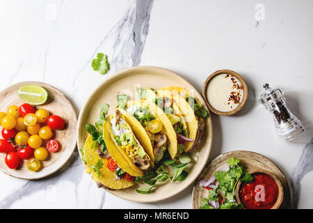 Auswahl an vegetarischen Mais Tacos mit Gemüse, Salat, Chili Pfeffer auf Keramikteller mit Tomaten und Sahne Saucen mit Zutaten serviert abov Stockfoto