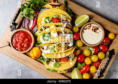 Auswahl an vegetarischen Mais Tacos mit Gemüse, Salat, Chili Pfeffer serviert auf Holz- Fach mit Tomaten und Sahne Saucen mit Zutaten oben Stockfoto