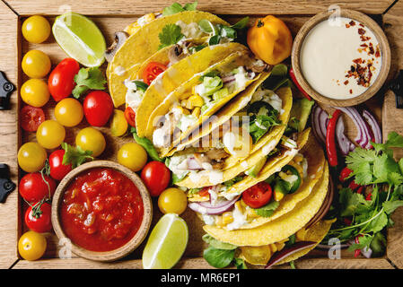 Auswahl an vegetarischen Mais Tacos mit Gemüse, Salat, Chili Pfeffer serviert auf Holz- Fach mit Tomaten und Sahne Saucen mit Zutaten oben. Stockfoto
