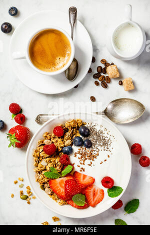 Gesundes Frühstück mit Kaffee und einer Schale mit hausgemachtem Müsli mit Joghurt und frischen Beeren auf weißem Hintergrund. Ansicht von oben, flach Stockfoto