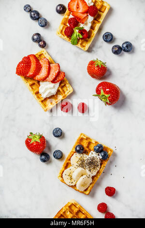 Traditionelle belgische Waffeln mit Schlagsahne und frischen Früchten und Beeren auf weißem Hintergrund. Flach, Ansicht von oben Stockfoto