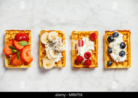 Traditionelle belgische Waffeln mit Schlagsahne und frischen Früchten und Beeren auf weißem Hintergrund. Flach, Ansicht von oben Stockfoto