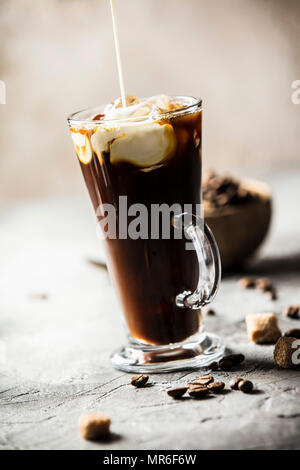 Eis Kaffee in ein hohes Glas mit Sahne über und Kaffeebohnen auf grauem Stein gegossen Stockfoto