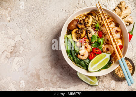 Asiatische Suppe mit Nudeln (Ramen), mit Miso einfügen, Sojasauce, grünen, Pilze und Garnelen Garnelen. Auf einem Tisch aus Stein, mit Stäbchen, Ingwer und Limette Stockfoto