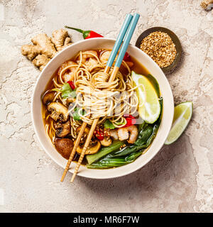 Asiatische Suppe mit Nudeln (Ramen), mit Miso einfügen, Sojasauce, grünen, Pilze und Garnelen Garnelen. Auf einem Tisch aus Stein, mit Stäbchen, Ingwer und Limette Stockfoto