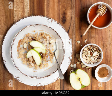 Eine Schüssel mit Bio Haferflocken Porridge mit in Scheiben geschnittenen Apfel oben und Schalen mit gehobelten Mandeln und Zimt. Stockfoto