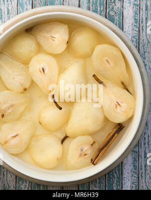 Eine Schüssel mit pochierten Birnen und einer Zimtstange in Sirup auf einem blauen strukturierten Hintergrund. Stockfoto