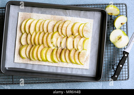 Eine ungekochte rechteckige Torte mit Reihen von Apple auf den Teig, ein Messer und schnitt Stücke vom Kochen von Apple. Stockfoto