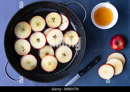 In Scheiben geschnittenen Äpfel in eine Pfanne mit Honig Sirup mit einer Schüssel mit Honig, einem Messer und einer in Scheiben geschnittenen Apfel. Stockfoto