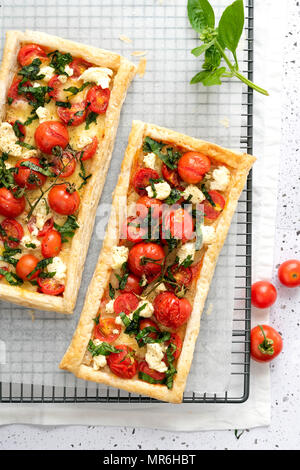 Zwei rechteckigen herzhafte Torten mit roten Kirschtomaten, boccocini Käse gefüllt und gehackte Basilikumblätter Kühlung auf einem Rack. Stockfoto