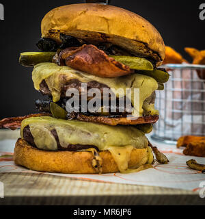 Unordentliche Beef Burger mit Käse, Speck, Champignons und Gurken. Mit einer Seite der süssen Kartoffeln serviert Stockfoto