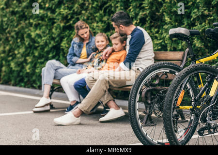Familie sitzt auf der Bank im Park, selektiver Fokus auf Fahrrädern in Vordergrund Stockfoto