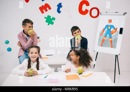 Multiethnische Gruppe von Kindern Äpfel essen beim Sitzen im Klassenzimmer während der Pause Stockfoto