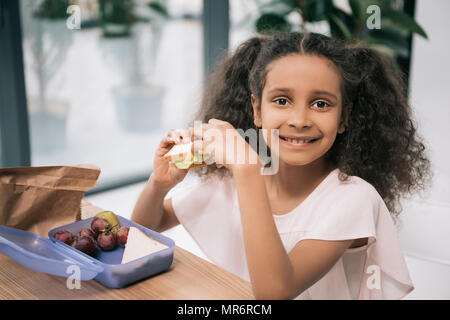 Cute afrikanische amerikanische Schülerin essen Sandwich und lächelnd an der Kamera am Mittagessen in der Schule Stockfoto