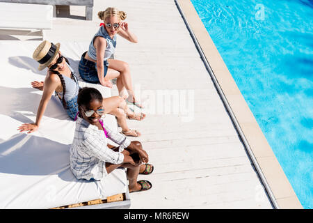 Junge schöne multiethnischen Frauen am Pool im Resort sitzen Stockfoto