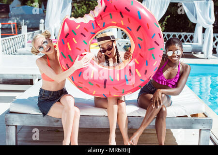Happy multiethnischen Frauen mit aufblasbaren Donut in der Nähe von Schwimmbad resort Posing Stockfoto