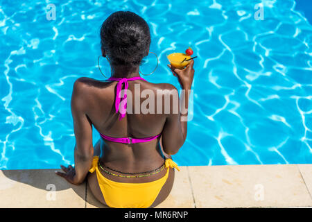 Afrikanische amerikanische Frau ruht mit Cocktail in der Nähe von Schwimmbad Resort Stockfoto