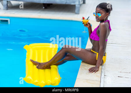 Afrikanische amerikanische Frau ruht mit Cocktail in der Nähe von Schwimmbad Resort Stockfoto