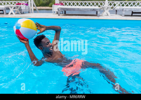 Junge glücklich afrikanische amerikanische Mann spielt mit Ball im Schwimmbad Stockfoto