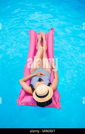 Junge Frau mit Strohhut, die schwimmend auf Luftmatratze im Pool Gesicht Stockfoto