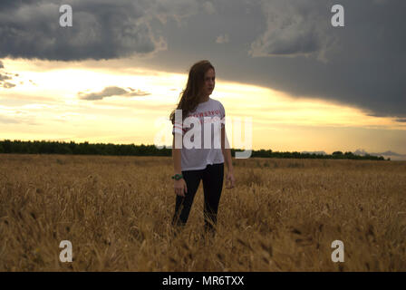 Junge Frau, Teenager, springen in einem Weizenfeld bei Sonnenuntergang Stockfoto