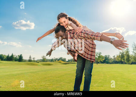 Afrikanische amerikanische Großvater, Enkelin piggyback Ride auf grünem Rasen mit Sonnenlicht Stockfoto