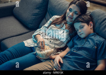 Little Boy fallen schlafend auf seiner Mutter Schulter beim Fernsehen auf der Couch Stockfoto