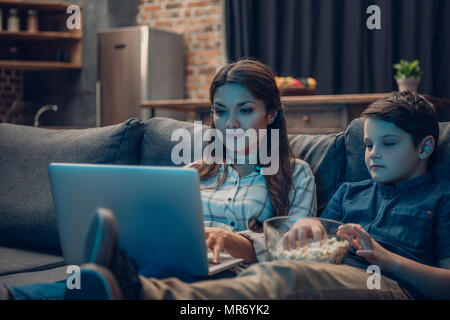 Kleinen Jungen und seiner schönen Mutter aufpassen Film auf Laptop und essen Popcorn, beim Sitzen auf der Couch Stockfoto