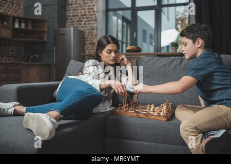 Little Boy und seine junge Mutter spielt Schach auf der Couch im Wohnzimmer. Stockfoto