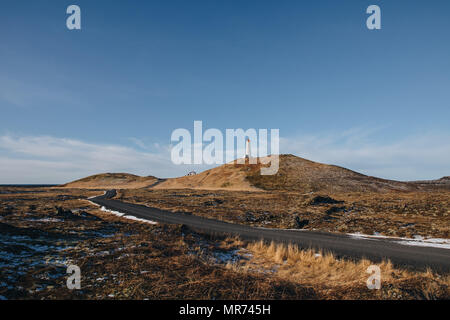 Leere Straße und Leuchtturm auf einem Hügel am sonnigen Tag in Island, valahnukamol, reykjanes Stockfoto