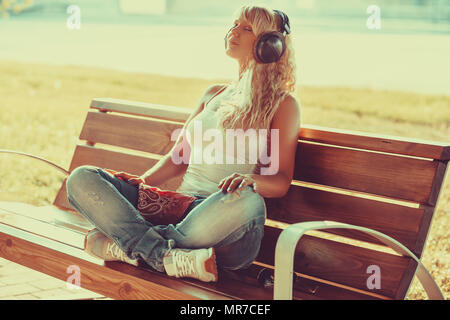 Junge Teenager Stil Frau sitzt auf der Bank am Morgen und hören Musik. Warme, sonnige Licht. Stockfoto