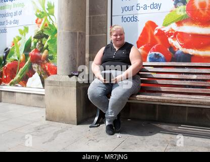 Eine übergewichtige Frau sitzt auf einer Bank ausserhalb des Co-op-Werbung gesundes Essen Stockfoto