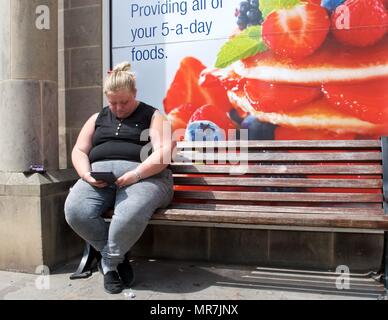 Eine übergewichtige Frau sitzt auf einer Bank ausserhalb des Co-op-Werbung gesundes Essen Stockfoto