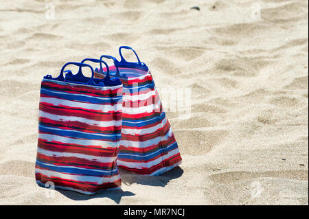 Nahaufnahme von zwei roten, weißen und blauen Taschen sitzen auf einem Sandstrand Stockfoto