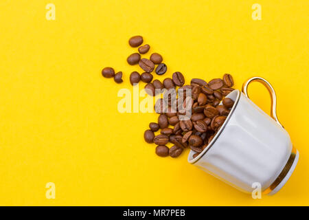 Verschüttete Kaffeebohnen aus einer Schale auf dem yellowbackground Stockfoto