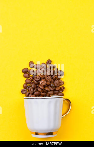 Verschüttete Kaffeebohnen aus einer Schale auf dem yellowbackground Stockfoto
