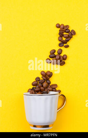 Verschüttete Kaffeebohnen aus einer Schale auf dem yellowbackground Stockfoto