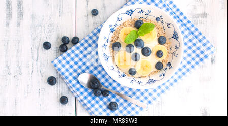 Eine Schüssel Müsli mit Blaubeeren und Himbeeren mit Joghurt auf einem Holztisch, gesundes Frühstück. Stockfoto