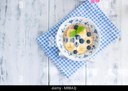 Eine Schüssel Müsli mit Blaubeeren und Himbeeren mit Joghurt auf einem Holztisch, gesundes Frühstück, Stockfoto