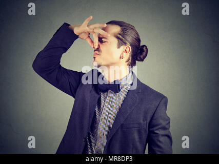 Angewidert Mann kneift Nase mit den Fingern blickt mit Abscheu etwas stinkt schlechter Geruch auf Wand Hintergrund isoliert. Menschliches Gesicht Ausdruck Reaktion Stockfoto