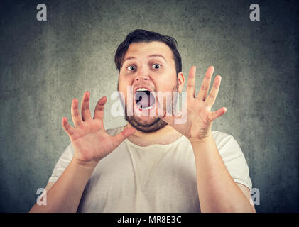 Chubby legerer Mann, Hände vor Gesicht und schrie mit Angst an Kamera suchen auf grauem Hintergrund. Stockfoto