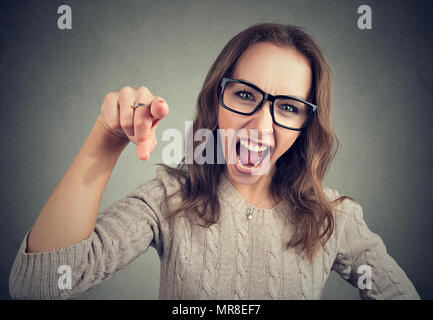 Junge Mädchen in Gläsern an Kamera und Geschrei in der Anklage zeigt sich wütend auf grauem Hintergrund. Stockfoto